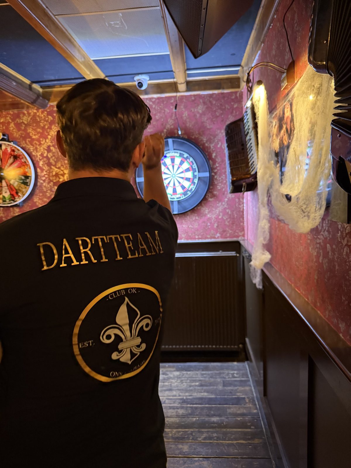 Iemand van het dartteam voor het dartbord, met het clubwapen op de rug van het shirt